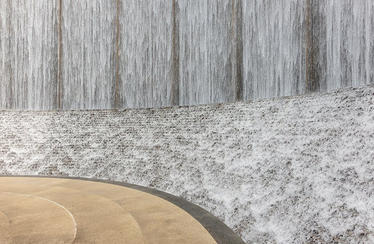 The curved waterfall wall at Gerald D. Hines Waterwall Park with live oak trees in Houston